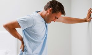 Ein Mann stützt sich mit Rückenschmerzen an der Wand ab. Gegen Rückenschmerzen StimaWEll.